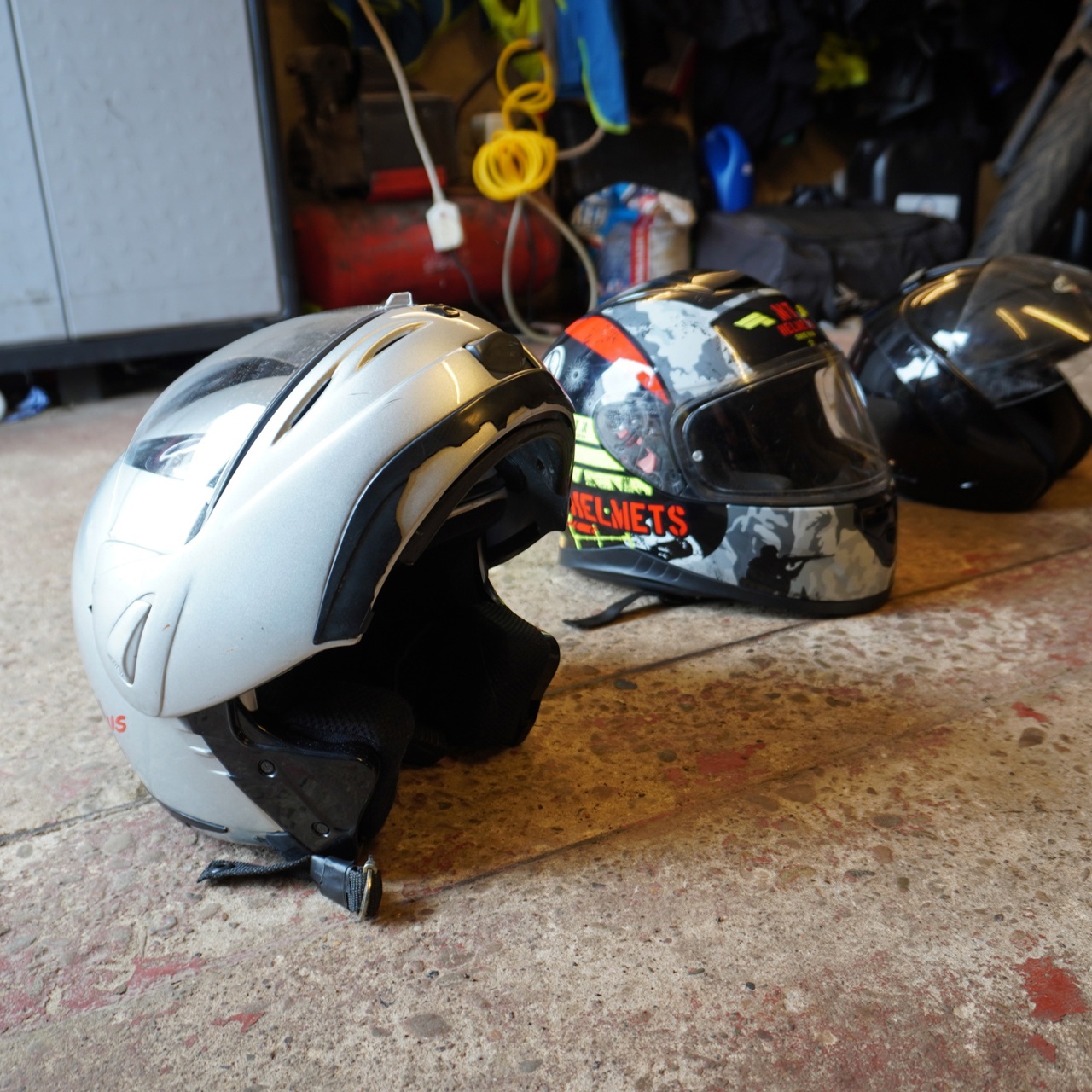 Three motorbike helmets on the floor of a garage