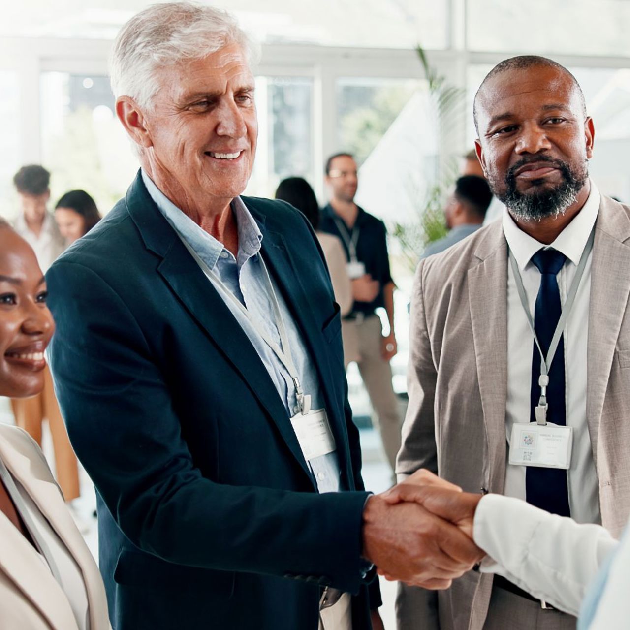 Grey haired man smiles and shakes hand with woman with two people looking on