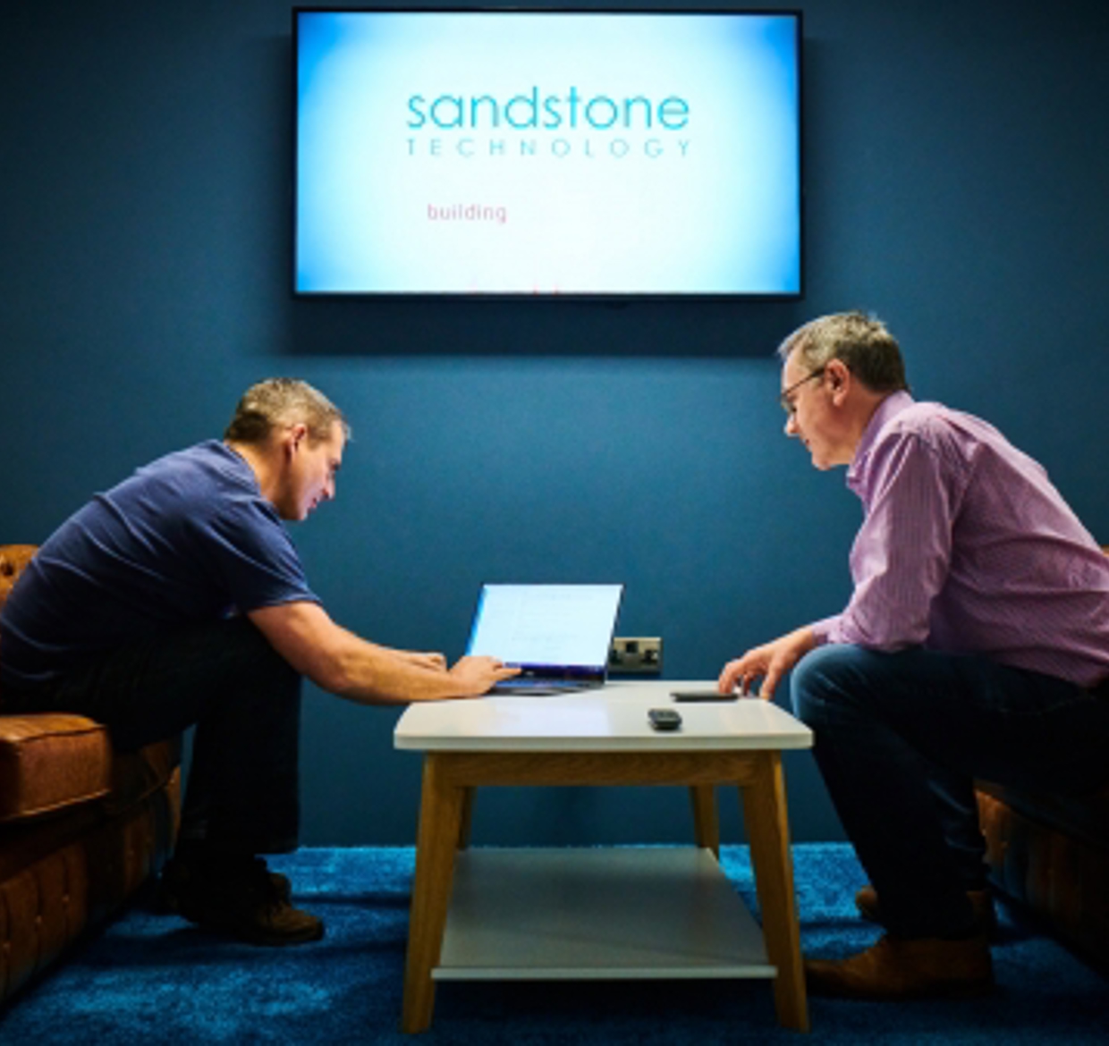 Two men sitting at a table with a laptop at Sandstone Technology