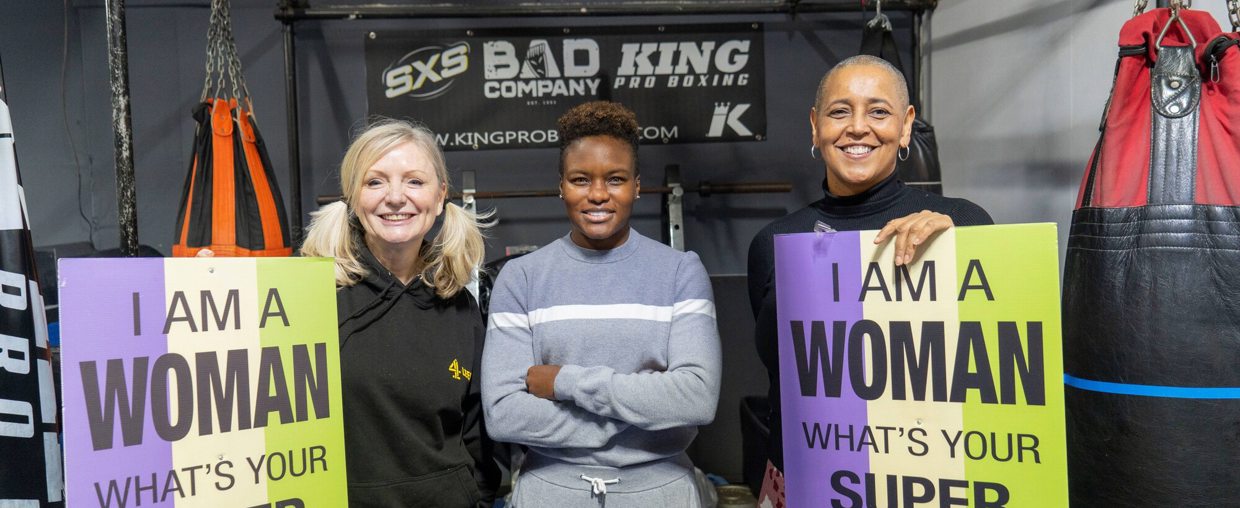 Tracy Brabin and Alison Lowe stand with boxer Nicola Adams holding signs saying 'I am a woman, what's your super power?'