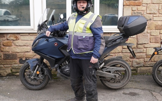 A man stood next to a parked motorbike, wearing full safety gear for riding