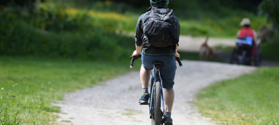 Man on bicycle wearing helmet and backpack is on a path heading in the opposite direction