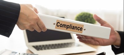 Two people passing a folder labelled 'Compliance'