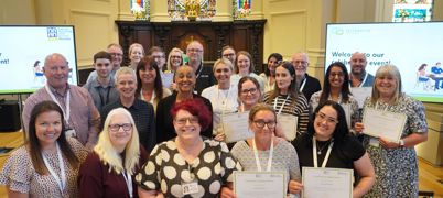 A group stood together in three rows with some holding certificates in a church backdrop