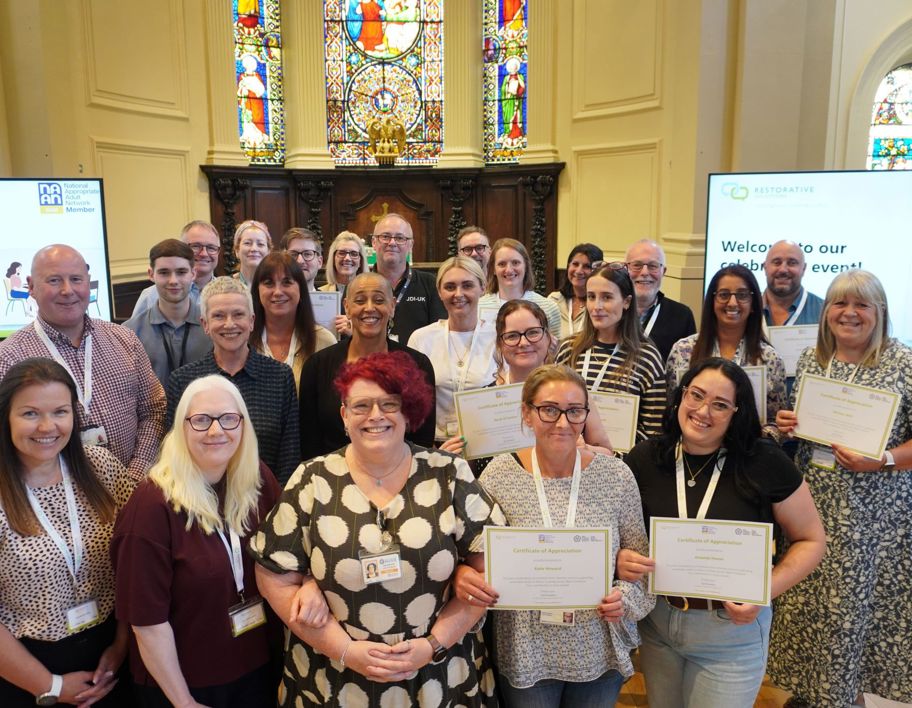 A group stood together in three rows with some holding certificates in a church backdrop