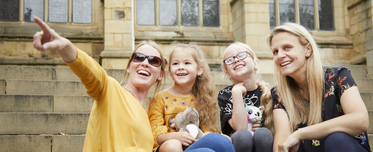 A Couple Of Women And Their Children Sat On Some Steps Of An Old Stone Building Enjoying The View