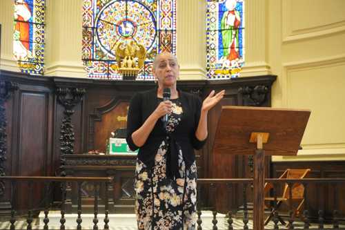 Deputy Mayor Alison Lowe speaking standing with a hand-held microphone with a church backdrop