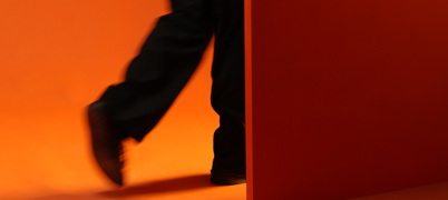 Person walking through a door with an orange backdrop