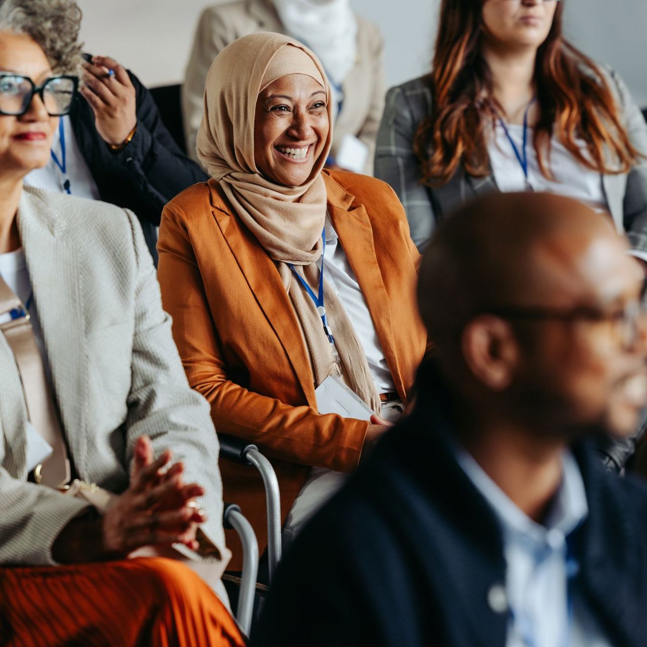 Sitting woman in orange jacket and headscarf smiles
