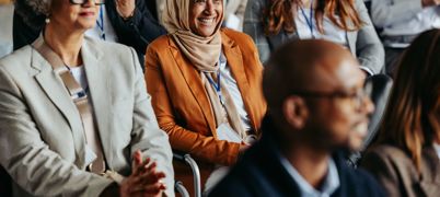 Sitting woman in orange jacket and headscarf smiles