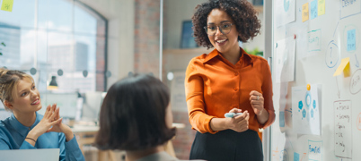 Colleagues in meeting room look at whiteboard full of post-it notes and ideas
