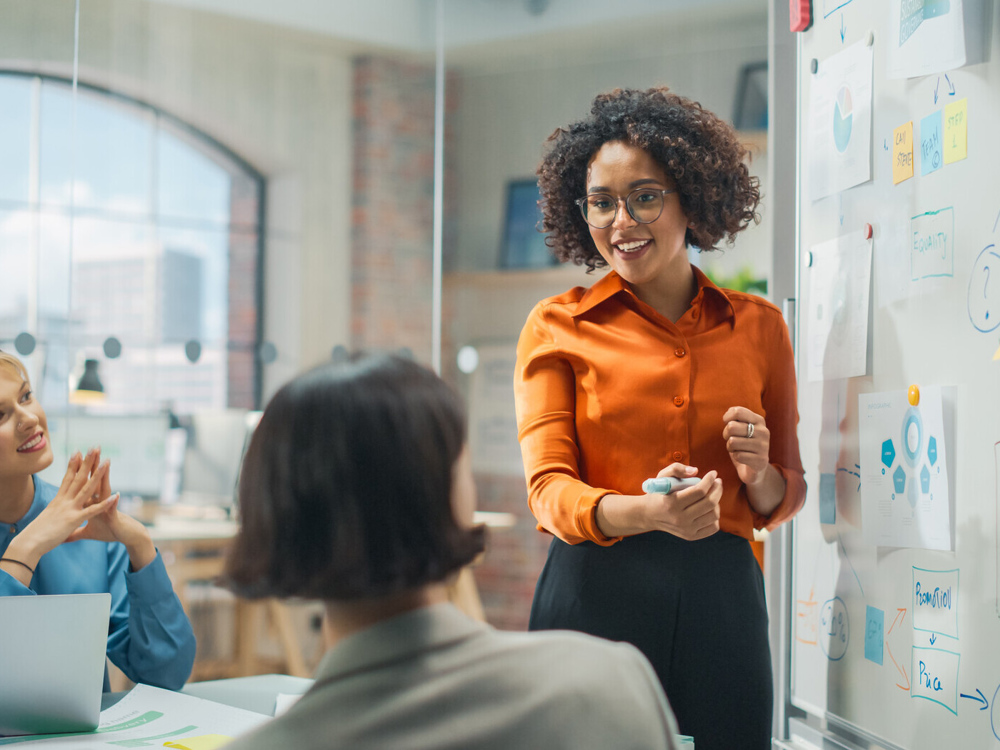 Colleagues in meeting room look at whiteboard full of post-it notes and ideas