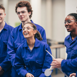 Group of manufacturing students smiling in protective eyewear and lab boilersuits