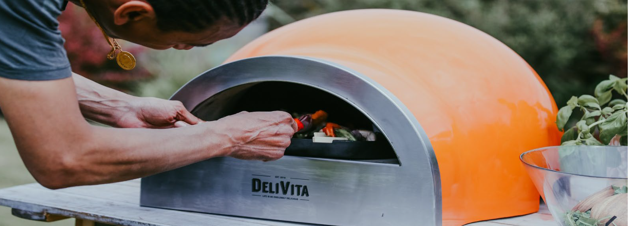 A man using a DeliVita wood-fired oven outdoors