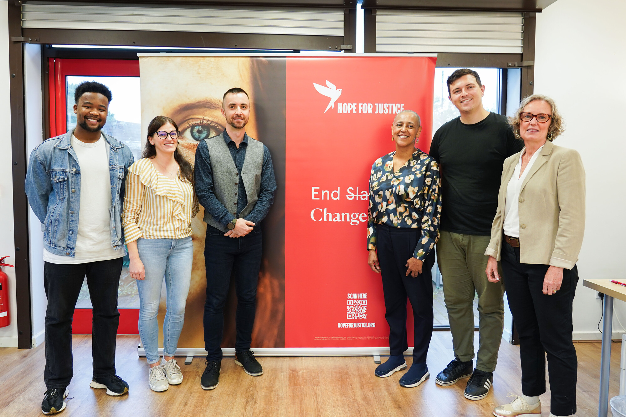 Photo of Alison Lowe and staff members from Hope for Justice. They are all stood in front of a Hope for Justice banner. They are smiling towards the camera.