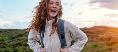 Young woman wearing fleece with hair blowing in wind looks happy on hike
