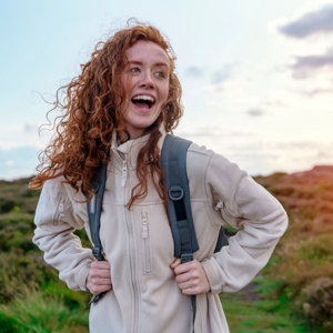 Young woman wearing fleece with hair blowing in wind looks happy on hike