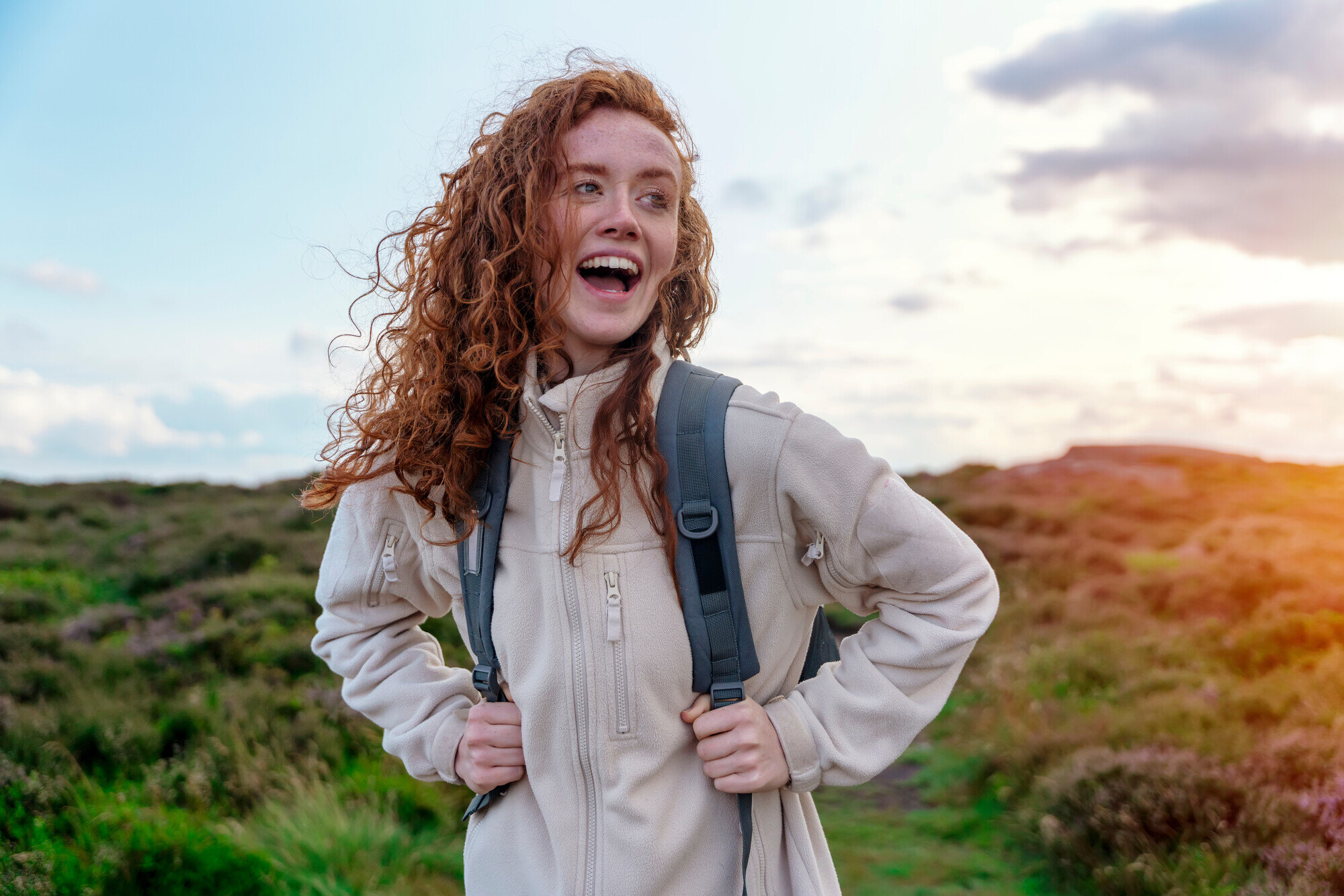 Young woman wearing fleece with hair blowing in wind looks happy on hike