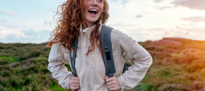 Young woman wearing fleece with hair blowing in wind looks happy on hike