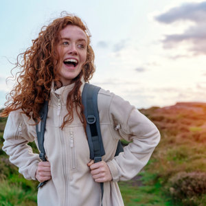 Young woman wearing fleece with hair blowing in wind looks happy on hike