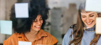 Two women sat in front of a window with post-its, smiling