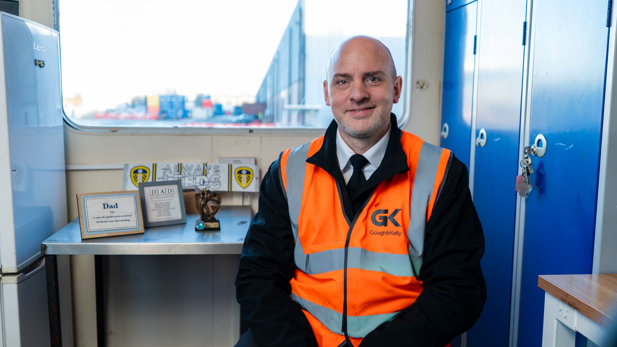 A man sat in an orange hi-vis jacket, smiling