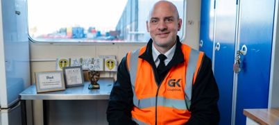 A man sat in an orange hi-vis jacket, smiling