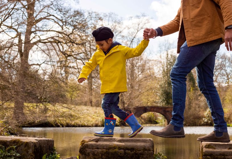 A young Sikh boy and his parent walking across stepping stones