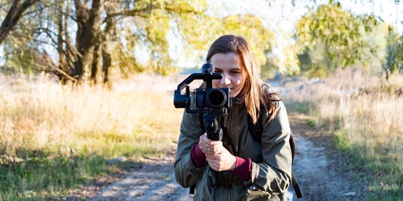 Female Videographer Holding A Gimbal With Camera Filming Outdoors On A Sunny Afternoon Stock